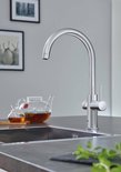 Chroom GROHE keukenkraan met gebogen uitloop, naast een glazen theepot met thee en een theeglas.