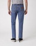 Achterkant van een man in een blauwe Wrangler jeans, met zwarte Converse sneakers.