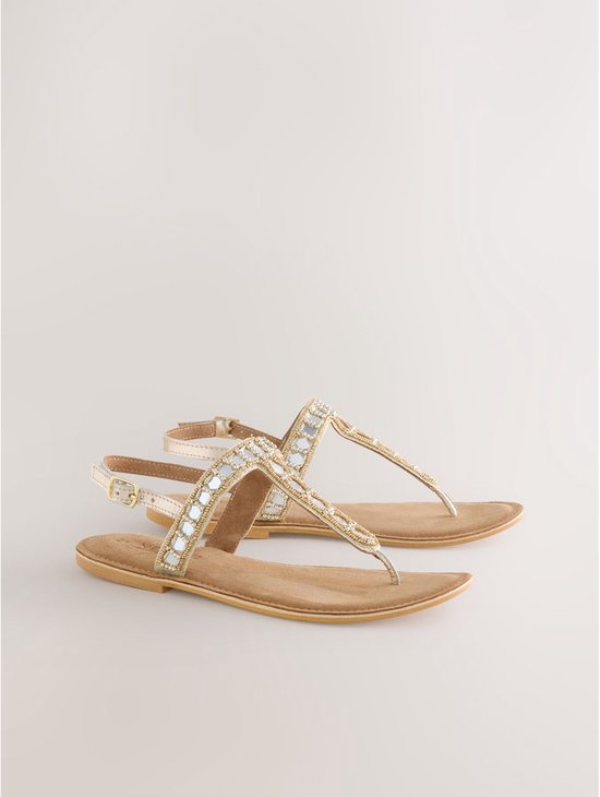Paar gouden sandalen met platte zool, versierd met parels en spiegeltjes op de bandjes.
