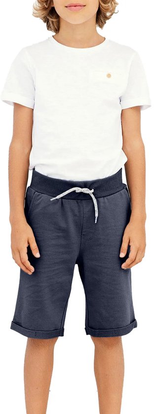 Jongen in een witte T-shirt en donkerblauwe shorts met trekkoord, opgerolde broekspijpen en een witte T-shirt.