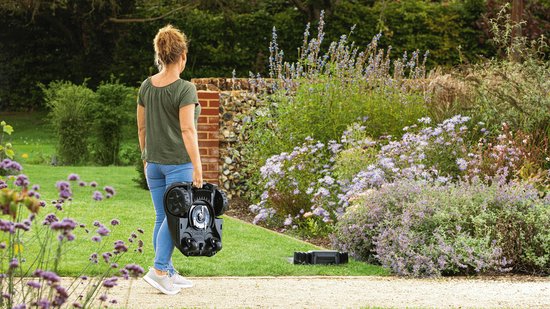 Vrouw met opvouwbare robotmaaier in een tuin met bloemen.