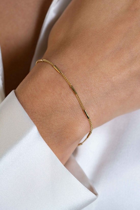 Close-up van een gouden armband met buisvormige schakels, gedragen om een pols van een vrouw.
