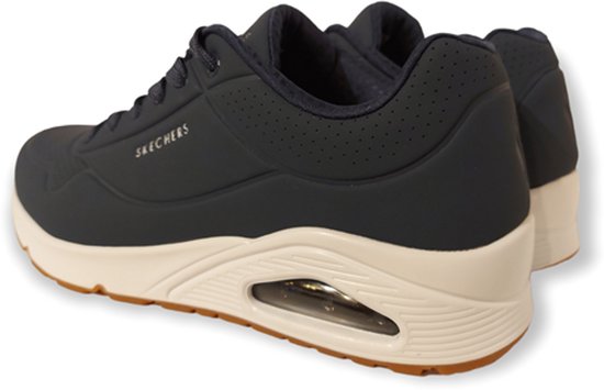 Sneaker Skechers bleu marine, vue arrière. Avec une semelle blanche, une bande de roulement marron et des coussinets d'air visibles. Logo SPERCHERS sur le côté.