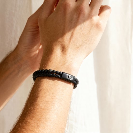 Zwarte gevlochten lederen armband met kralen van zwarte lavasteen en mat zwart, gedragen om een mannenpols.
