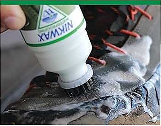 Hand met groene Nikwax fles brengt reiniger aan op schoen met borstel.