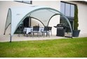 Een Coleman partytent met tafel en stoelen, naast een huis met een barbecue.