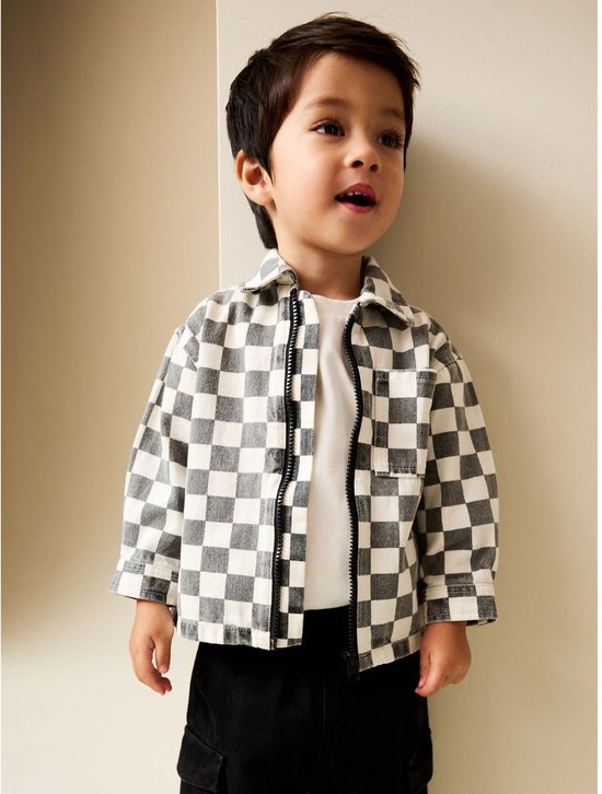 Jongen in een grijs-wit geblokt overshirt over een wit T-shirt met een zwarte broek.