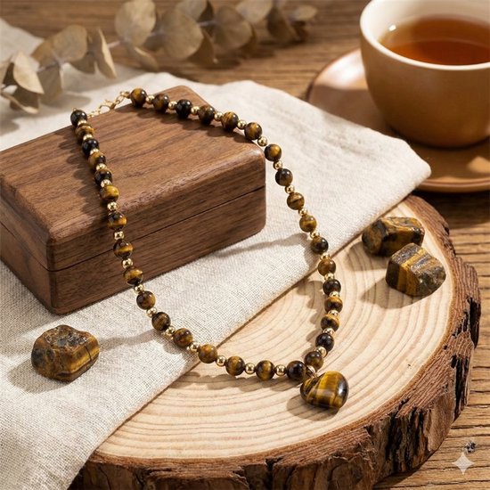 Bruin-zwarte kralenketting met hartvormige tijgeroog hanger en gouden accenten, op een houten ondergrond.