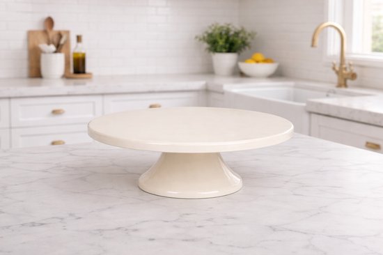 Plateau à gâteau en céramique blanc cassé avec un pied torsadé, posé sur un plan de travail en marbre.