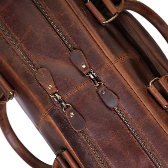 Close-up van de dubbele ritssluitingen met leren lipjes op een verweerde bruine leren tas.