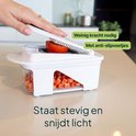 Witte groentesnijder met een tomaat die wordt gesneden, met rode blokjes groenten in de opvangbak. Tekst 'Staat stevig en snijdt licht'.