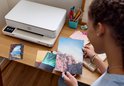 Jonge vrouw met vlecht met clipjes, bekijkt foto's bij een witte HP Envy printer.