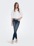 Vrouw met een witte blouse, een beige riem en een donkerblauwe skinny jeans met rafelige zoom.