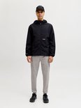 Man met zwarte jas, grijze joggingbroek, pet en sneakers. Frontaal zicht op witte achtergrond.