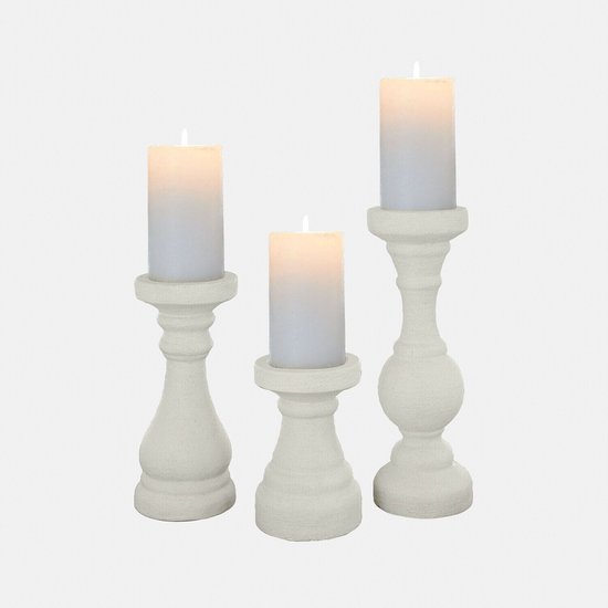 Drie witte, robuuste kandelaars met gedetailleerd houtsnijwerk, met brandende kaarsen.