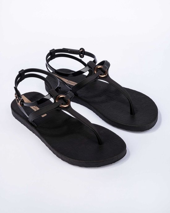 Zwarte Ipanema slippers met bandjes en gouden ringen, met subtiel patroon.