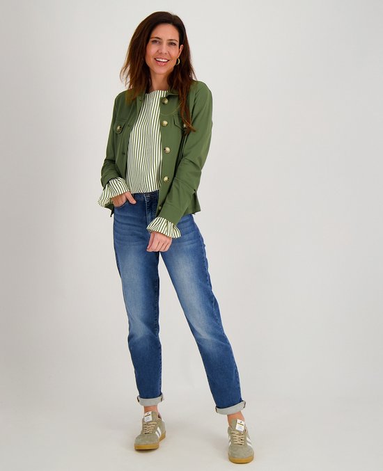 Vrouw in groene jas, gestreepte top met ruches en spijkerbroek.