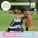 Vrouw in bruine jas met een hond in een grijze hondenbuggy in een park. De buggy ondersteunt tot 77 lbs (34.9 kgs).
