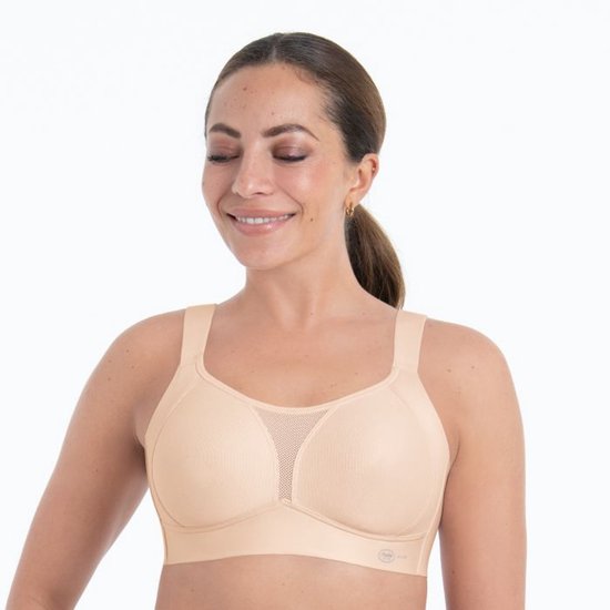 Frontaal aanzicht van een lachend model in een beige sportbeha met mesh-detail op de cups en brede bandjes.