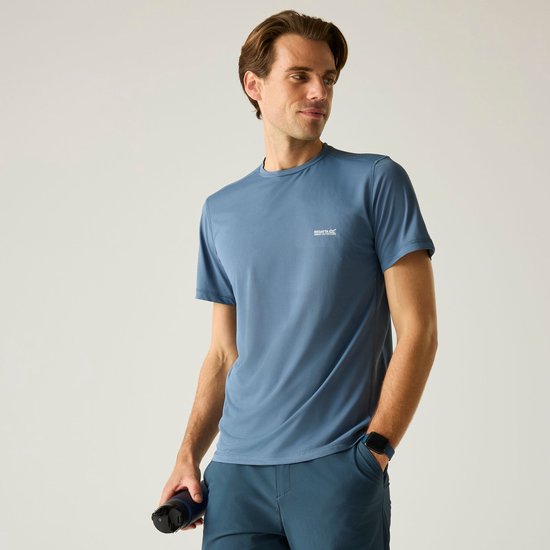 Man draagt een blauw T-shirt met korte mouwen, een donkerblauwe broek en horloge, met fles in de hand.