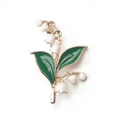 Gouden broche met witte lelietjes van dalen en groene bladeren, op een witte achtergrond.