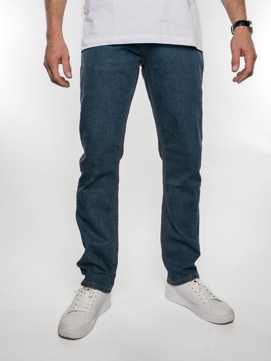 Man in een wit T-shirt en spijkerbroek met een middenblauwe wassing, gedragen met witte sneakers.