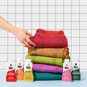 Een stapel gekleurde spijkerbroeken, van rood tot paars. Op de voorgrond staan flesjes Rit Dye in bijpassende kleuren.