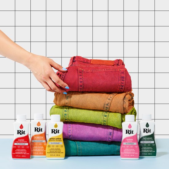 Een stapel gekleurde spijkerbroeken, van rood tot paars. Op de voorgrond staan flesjes Rit Dye in bijpassende kleuren.