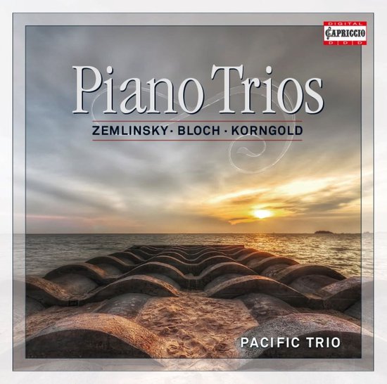 Albumhoes met titel 'Piano Trios' en vermelding van ZEMLINSKY, BLOCH, KORNGOLD en PACIFIC TRIO. Zonsondergang boven zee met golfbreker op voorgrond.