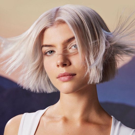Model met kort, platinum blond haar dat wappert, draagt witte tanktop.