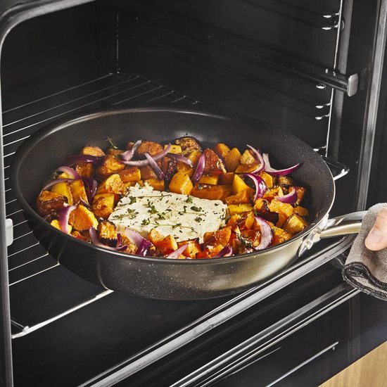Man plaatst een pan met geroosterde groenten en kaas in een oven.