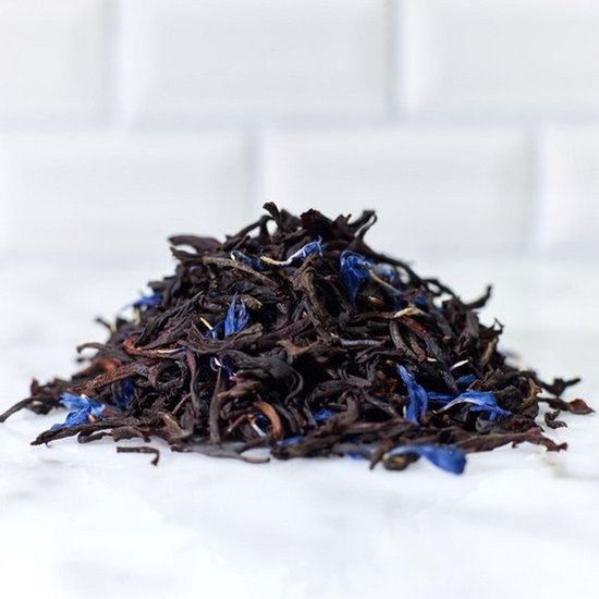 Losse Earl Grey thee met gedroogde blauwe korenbloembloesems op een wit marmeren oppervlak.