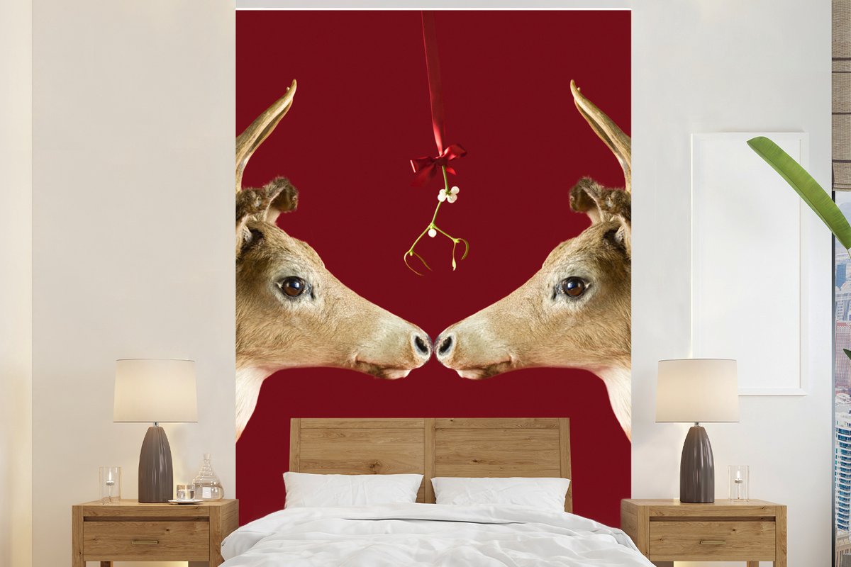 Behang - Fotobehang Twee rendieren onder een maretak rode achtergrond - Breedte 160 cm x hoogte 240 cm