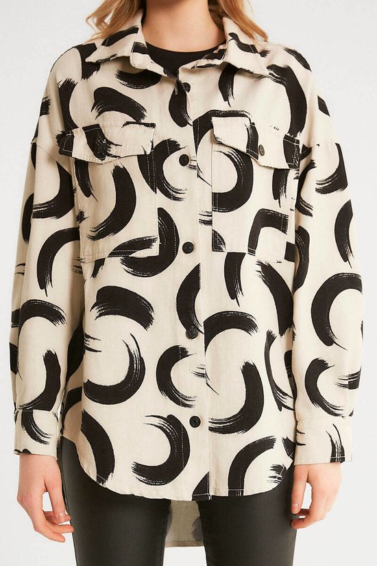 Close-up van de voorkant van een beige oversized jas met zwarte kwastprint, knopen en borstzakken.