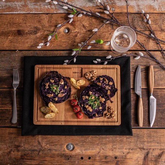 Boska steakmessen met houten handvat naast een houten plank met rode kool en gegarneerde salades.