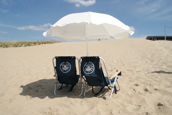 Twee donkerblauwe campingstoelen onder een witte parasol op het strand, met duinen op de achtergrond.