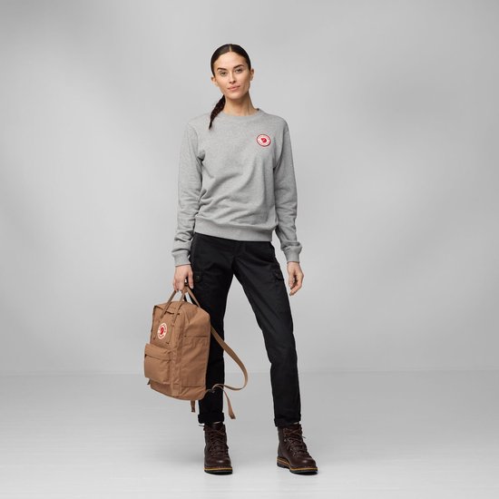 Vrouw met een bruine Fjallraven Kanken rugzak, grijze sweater en zwarte broek.