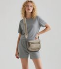 Model met blonde krullen draagt een beige Eleganci heuptas van zacht vegan leer met een verstelbare schouderband met witte bies.