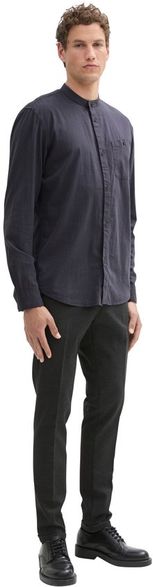 Man met donkerblauw overhemd met opstaande kraag en donkere broek.