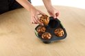 Handen plaatsen een chocoladechipmuffin in een donkergrijze siliconen muffinvorm.