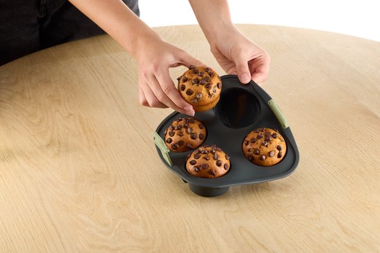 Handen plaatsen een chocoladechipmuffin in een donkergrijze siliconen muffinvorm.