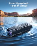 Zwarte Soundcore speaker in het water met splash-effect, tegen de achtergrond van een woestijnlandschap.