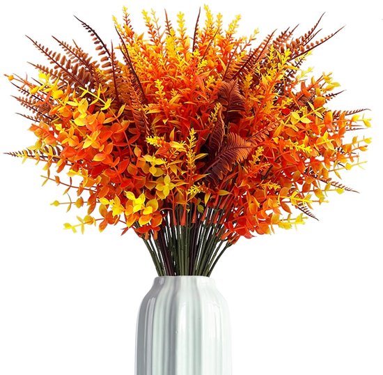 Un bouquet de plantes artificielles oranges, jaunes et brunes avec de longues feuilles fines et des feuilles en forme de plume dans un vase blanc.