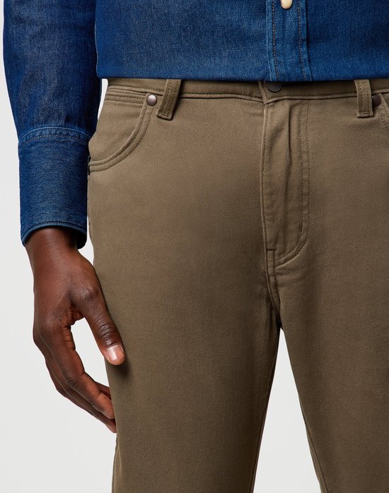 Close-up van de voorkant van een olijfgroene Wrangler broek, gedragen door een man.