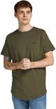 Man met tatoeages op zijn arm draagt een olijfgroene t-shirt met korte mouwen en ronde hals, met een klein logo op de borst, staand.