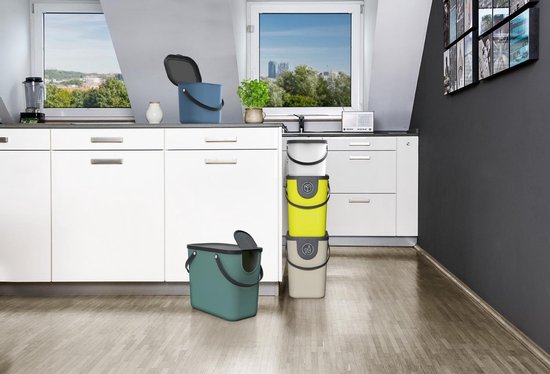 Keuken met aanrecht en lades, met groene en blauwe afvalbakken. Drie gestapelde bakken: wit, geel en grijs.