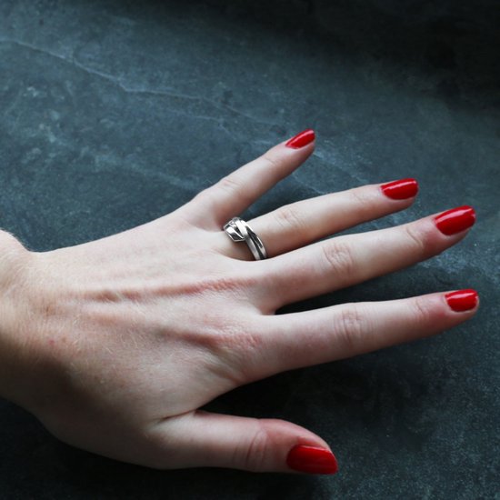 Zilverkleurige ring met een knoopmotief, gedragen door een hand met rode nagellak.