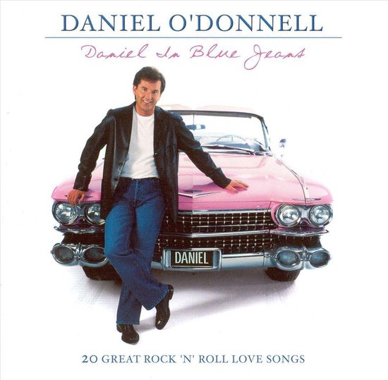 Daniel O'Donnell in blauwe jeans en een zwart jack leunt op een roze klassieke auto. Titel: Daniel In Blue Jeans.