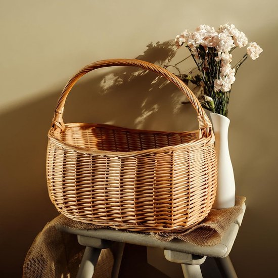 Panier rond en osier avec une anse, posé sur un tabouret avec un vase de fleurs.