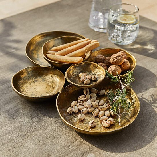 Een antiekgouden schaal met pistachenoten, grissini, walnoten en rozemarijn, met een glas water op de achtergrond.